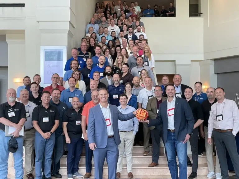 Large group of professionals posing on steps in a building lobby for a group photo at a conference.