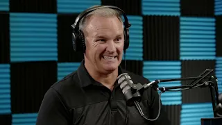 A person wearing headphones and speaking into a microphone in a soundproofed studio with blue and black acoustic panels on the wall.